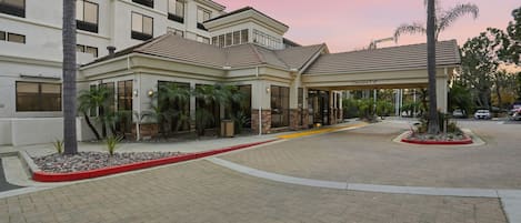 A hotel entrance with a covered walkway, palm trees, and a clear sky.