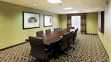 A conference room with a long table, six chairs, framed artwork on the walls, and patterned carpet.