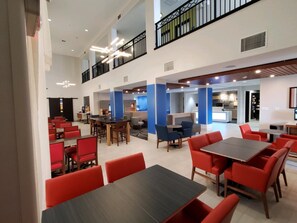 A spacious indoor area with multiple seating arrangements, including tables and chairs, and a kitchen area in the background. - Holiday Inn Express & Suites Phoenix - Glendale Sports Dist by IHG (Glendale)