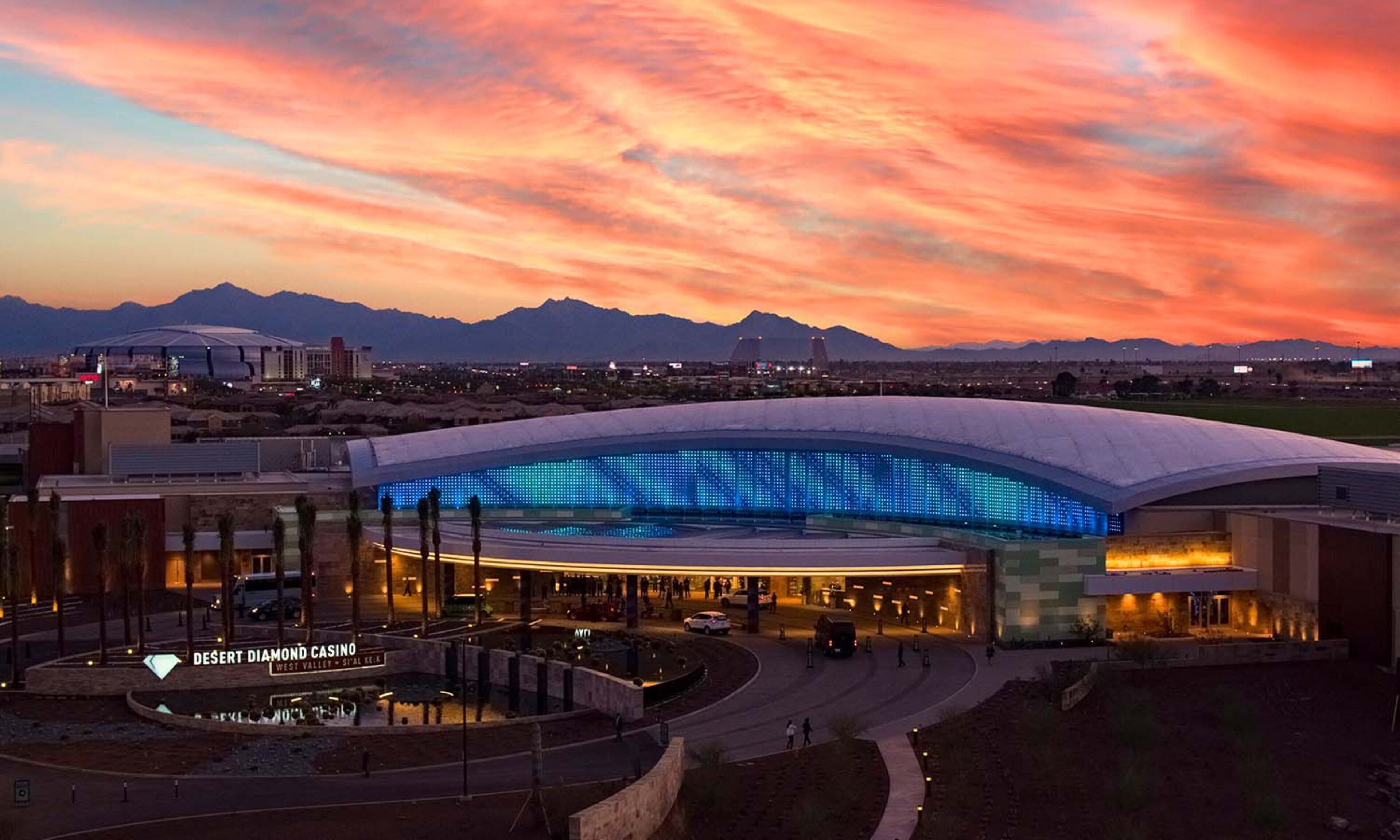 A large, modern building with a curved roof, surrounded by a landscaped area and a desert landscape in the background.
