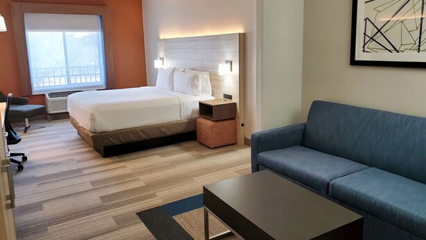 Quarto de hotel com cama, escrivaninha, cadeira, sofá e um quadro na parede.