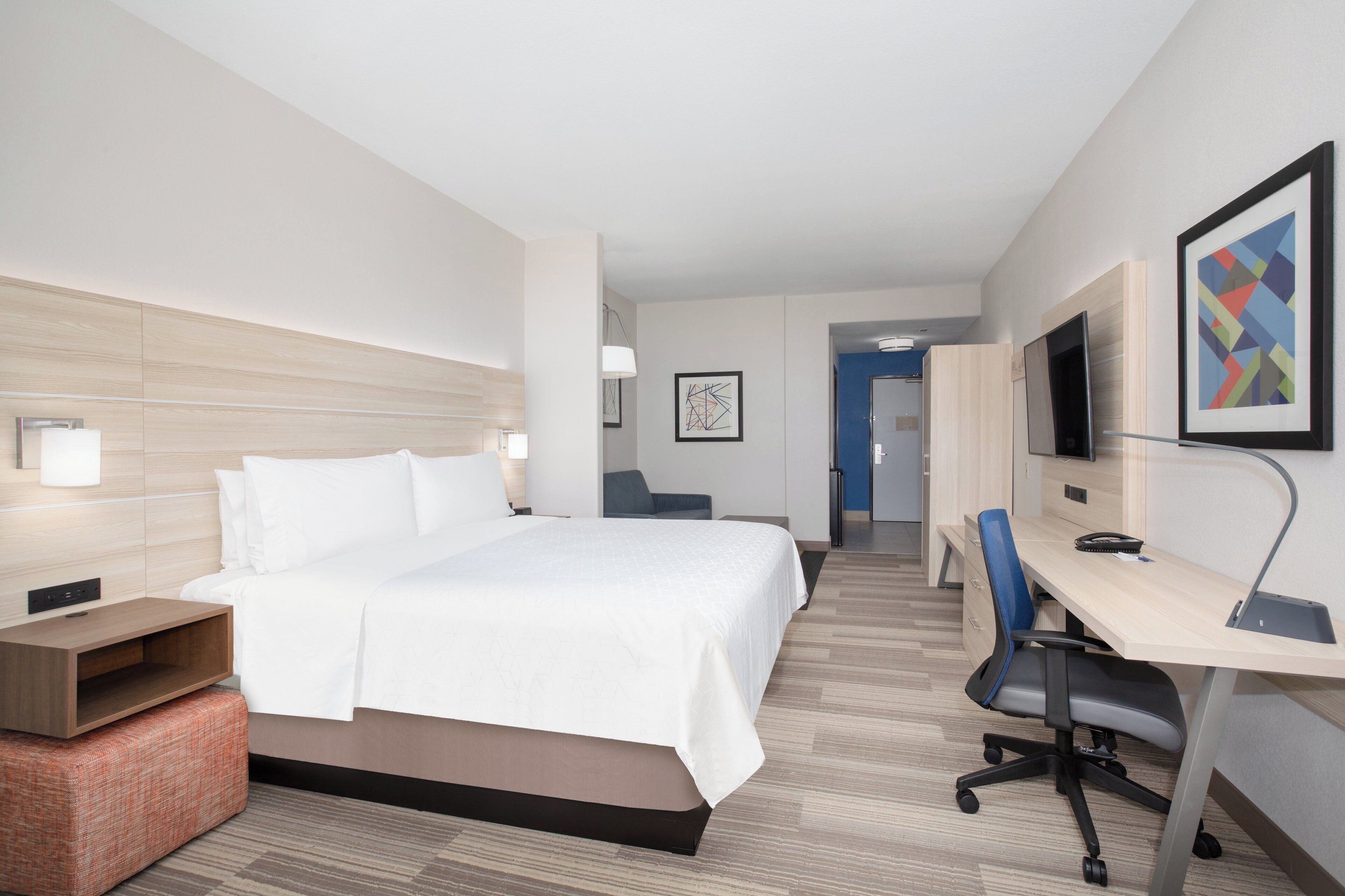 Habitación de hotel con cama, escritorio, silla y televisor en la pared.