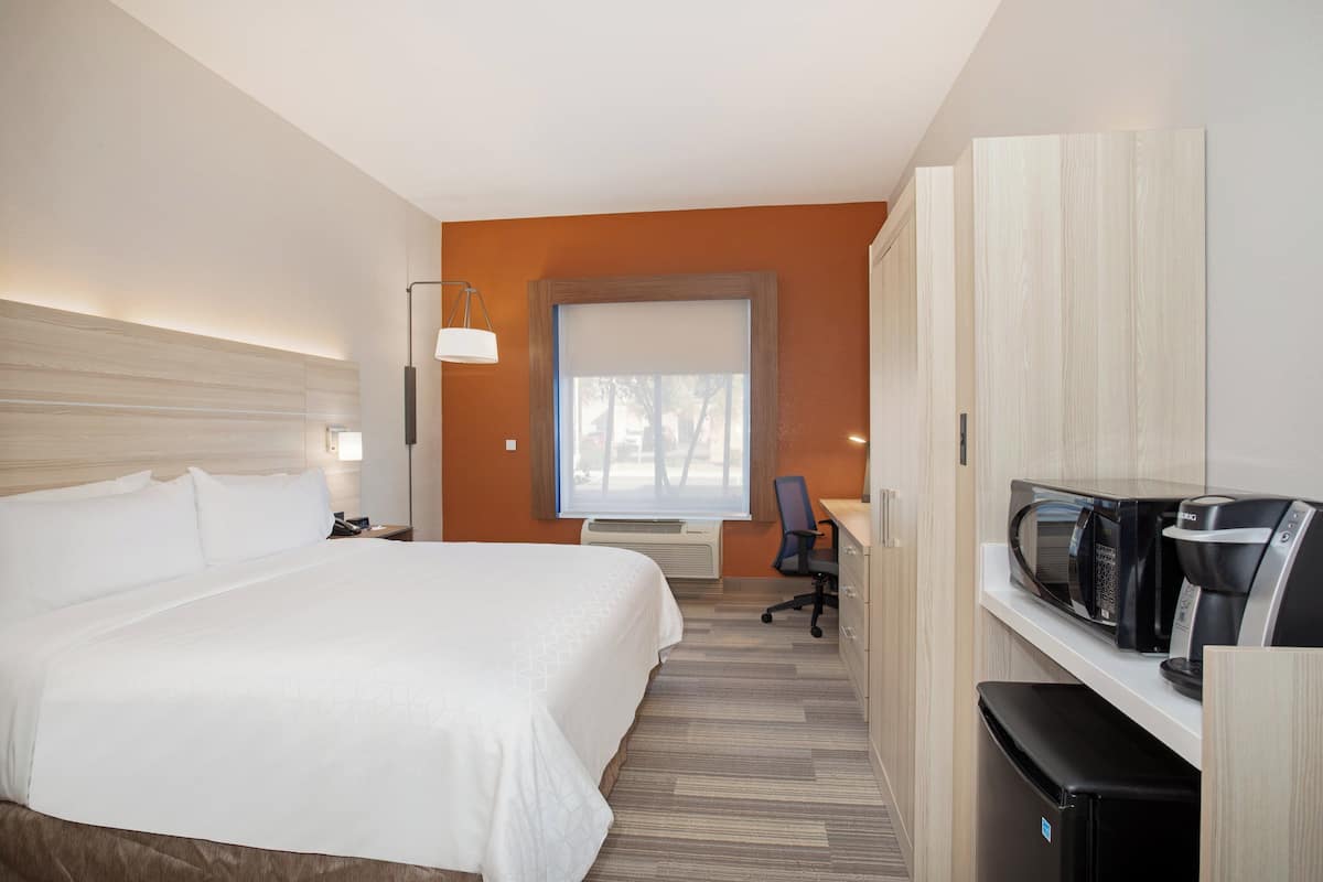 A hotel room with a large bed, a desk with a computer, a microwave, and a refrigerator.