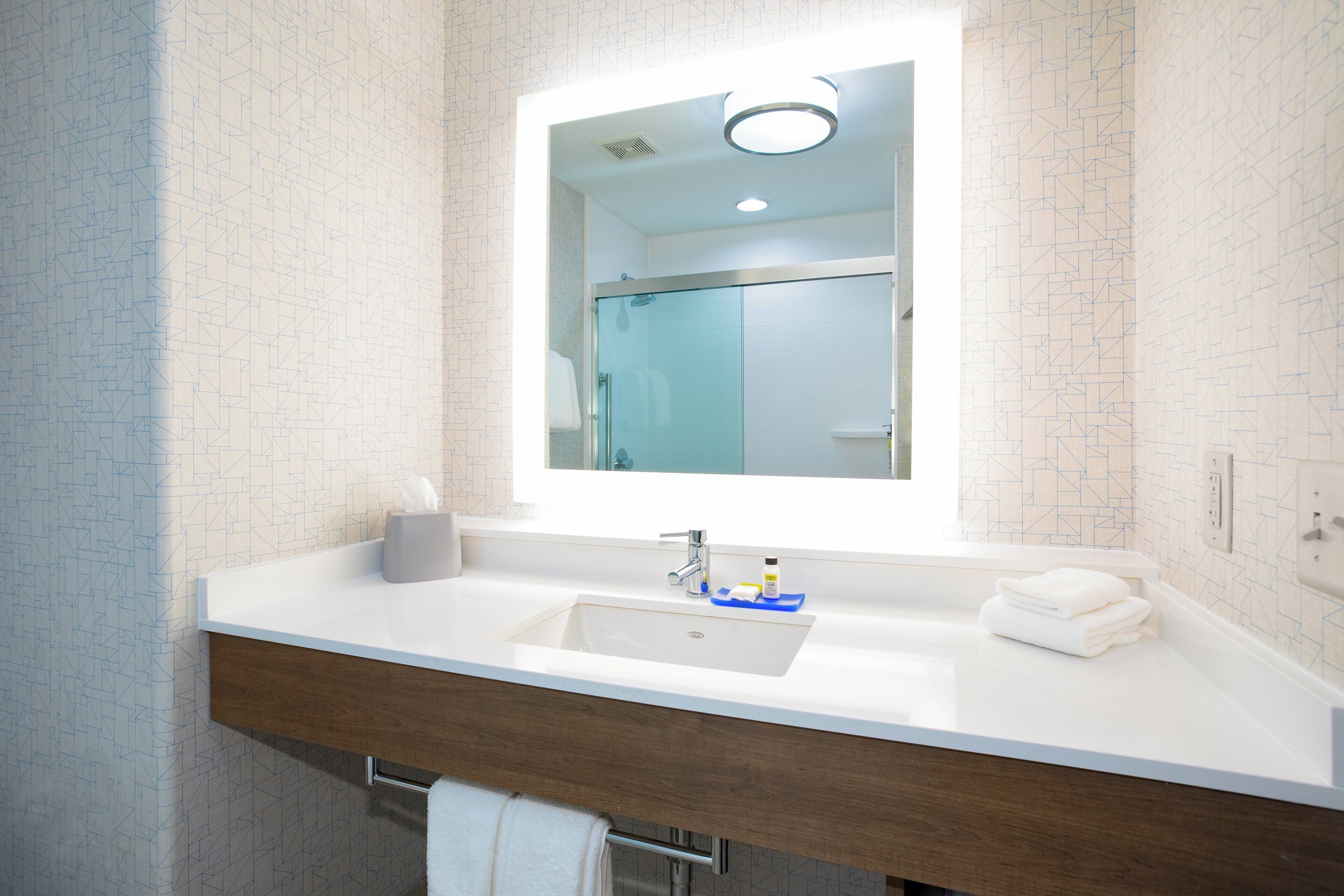 Une salle de bain moderne avec un grand miroir, un lavabo blanc et un porte-serviettes.