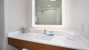 Casa de banho com lavatório branco, espelho e chuveiro visível no reflexo.