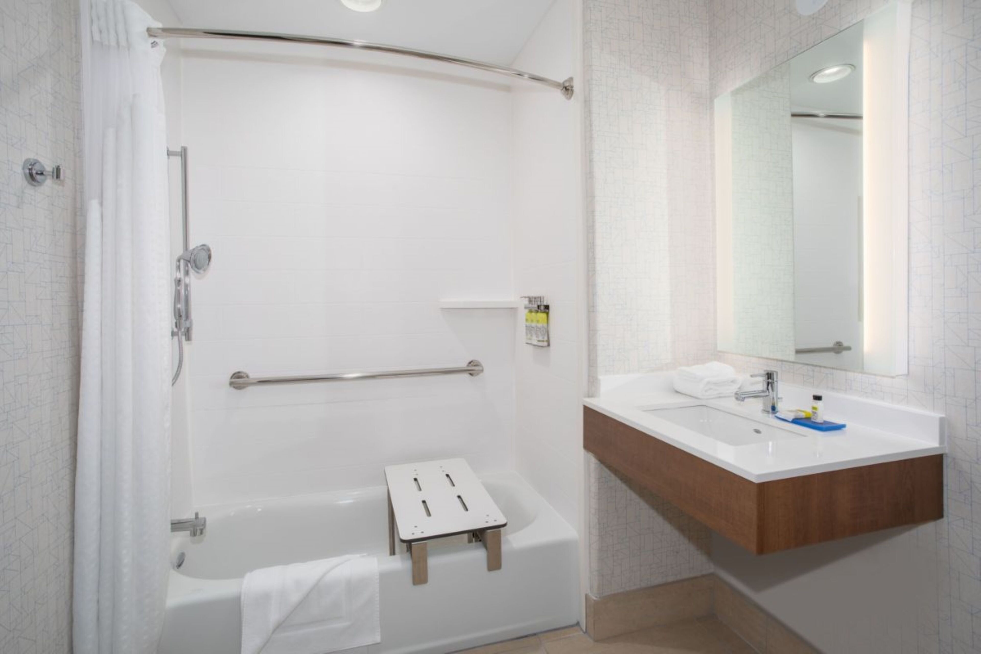 Un baño moderno con ducha a ras de suelo, bañera, tocador con espejo y un perchero para toallas.