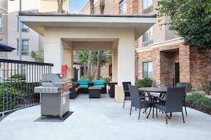 Un área de patio al aire libre con una parrilla, asientos y vistas de los edificios circundantes.