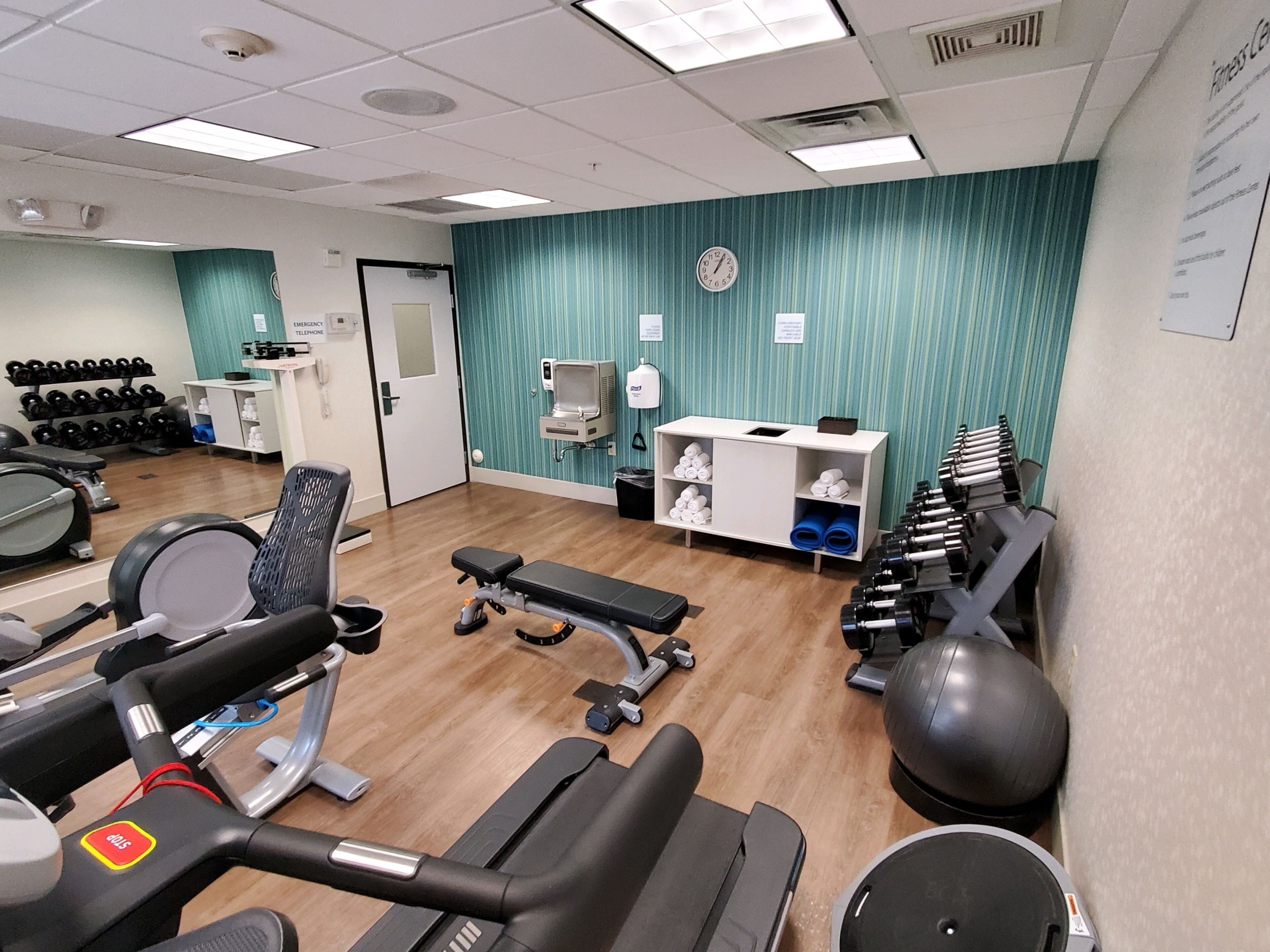 Ein Fitnessraum mit Trainingsgeräten, einer Rezeption und einer Wanduhr.