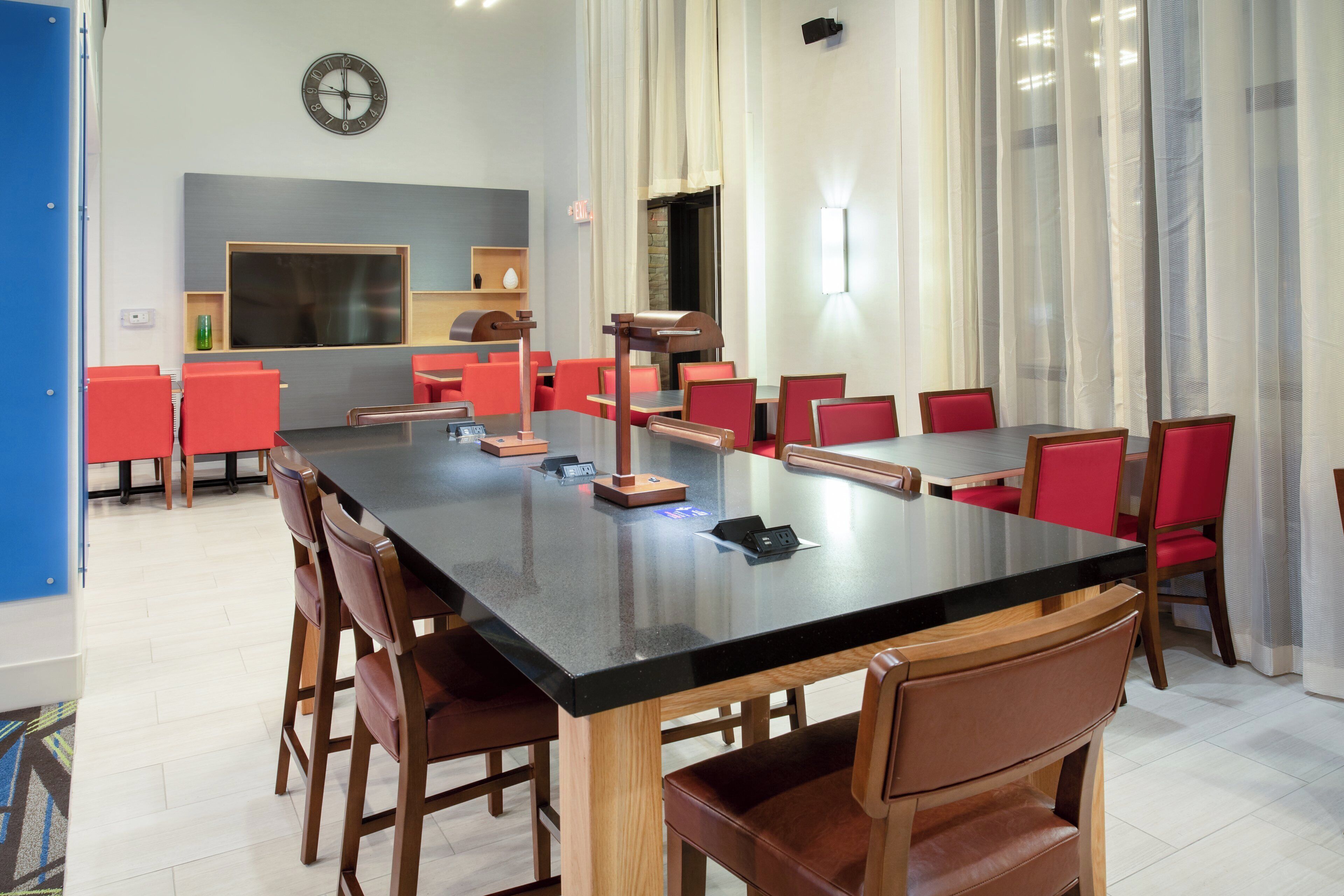 Una sala conferenze con un lungo tavolo, sedie rosse, un orologio appeso al muro e uno schermo televisivo.