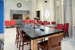 Une salle de conférence avec une longue table, des chaises rouges, une horloge au mur et un écran de télévision.
