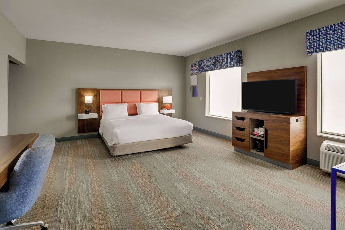 Una habitación de hotel con cama, escritorio, televisión y ventana.