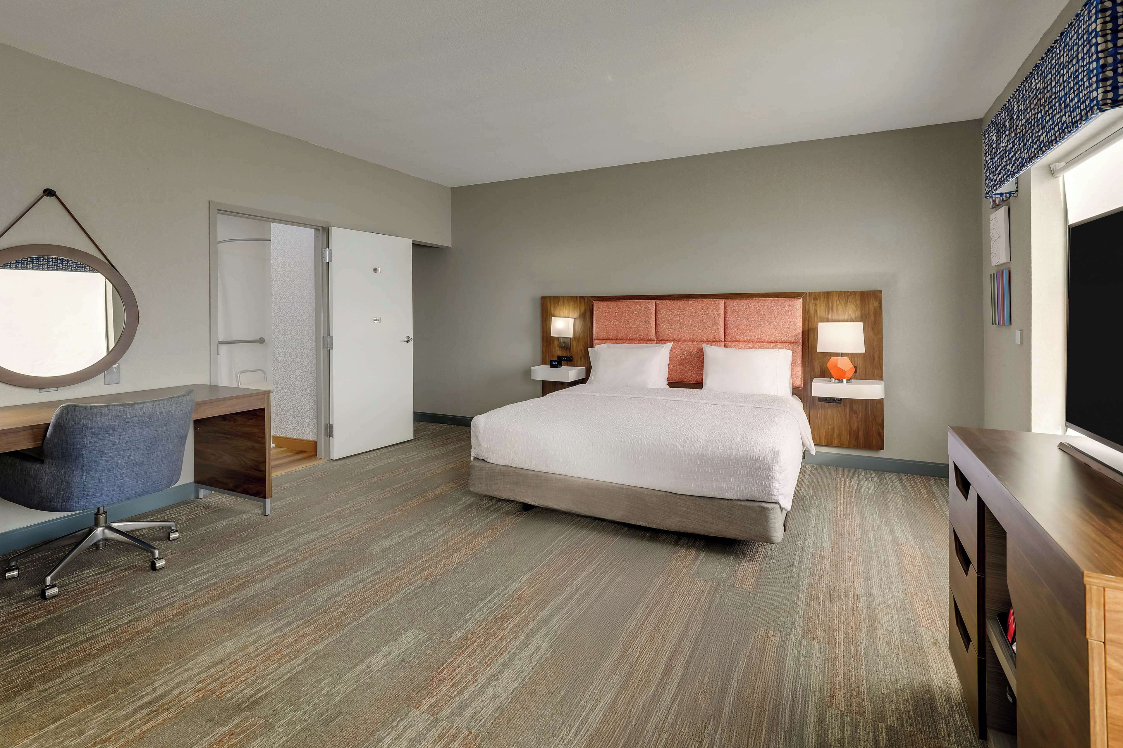 A hotel room with a bed, desk, chair, and a TV.