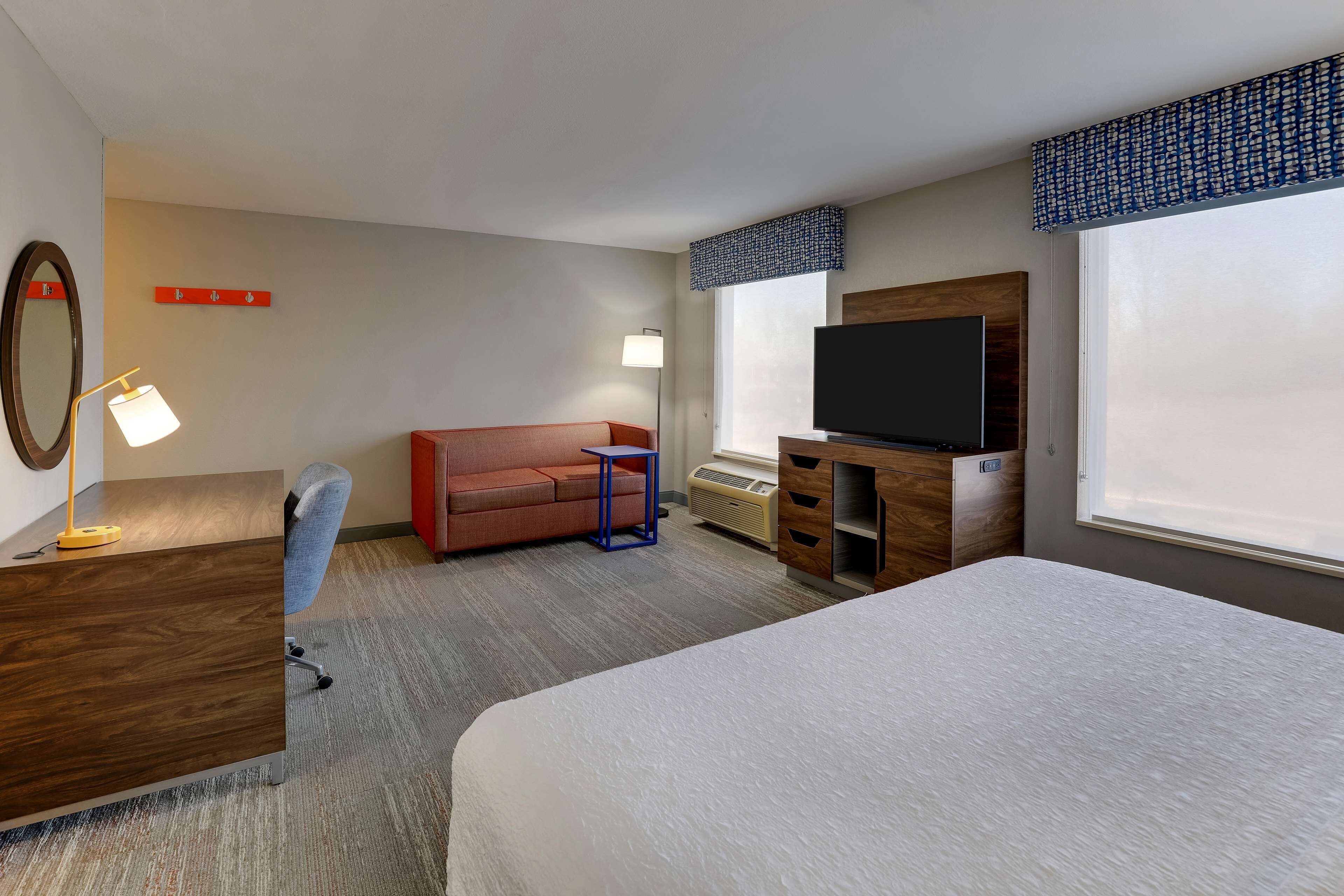 Une chambre d’hôtel équipée d’un lit, d’un bureau, d’une chaise, d’un canapé, d’une télévision et d’une fenêtre avec des stores.