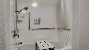 A modern bathroom with a bathtub, shower, and handrails.