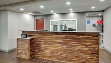 A hotel reception desk with a wooden panel design, a sign indicating Hilton Honors, and a framed picture of a farm on the wall.