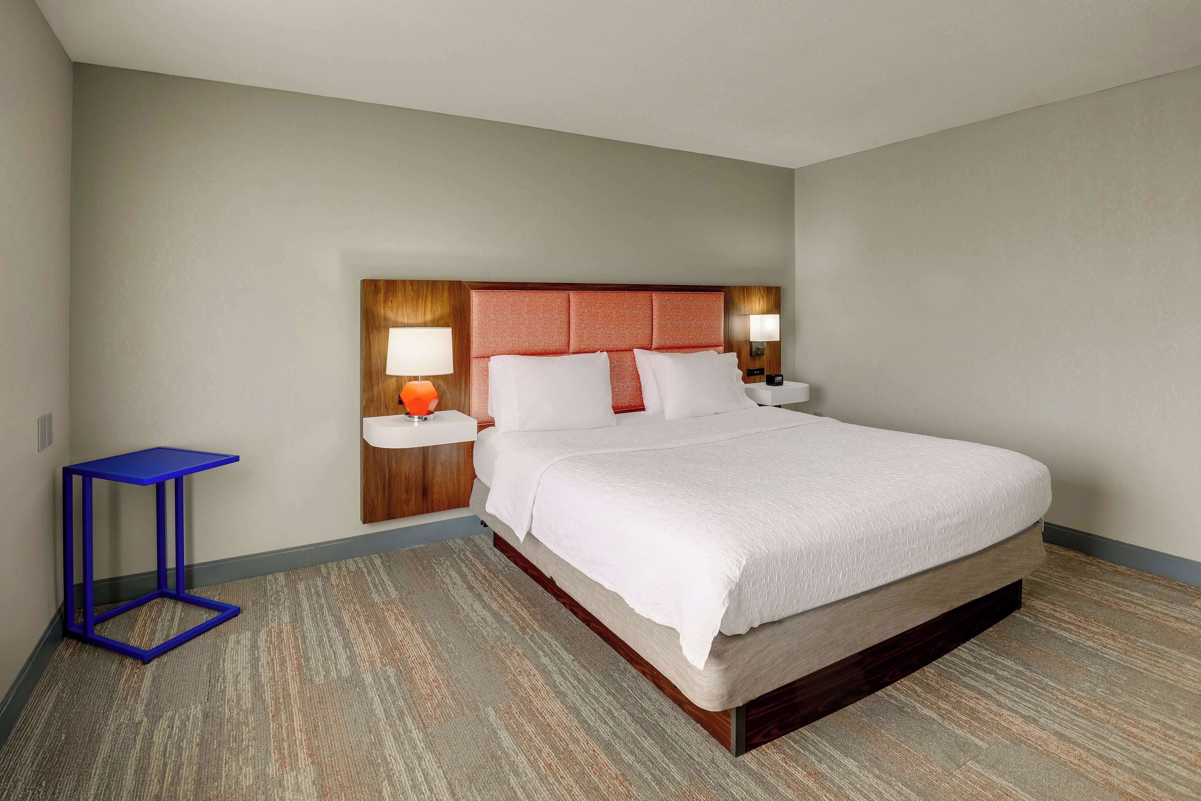 A hotel room with a large bed, a small side table, and a nightstand with a lamp.
