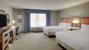 A hotel room with two beds, a desk with a TV, a chair, and a window with curtains.