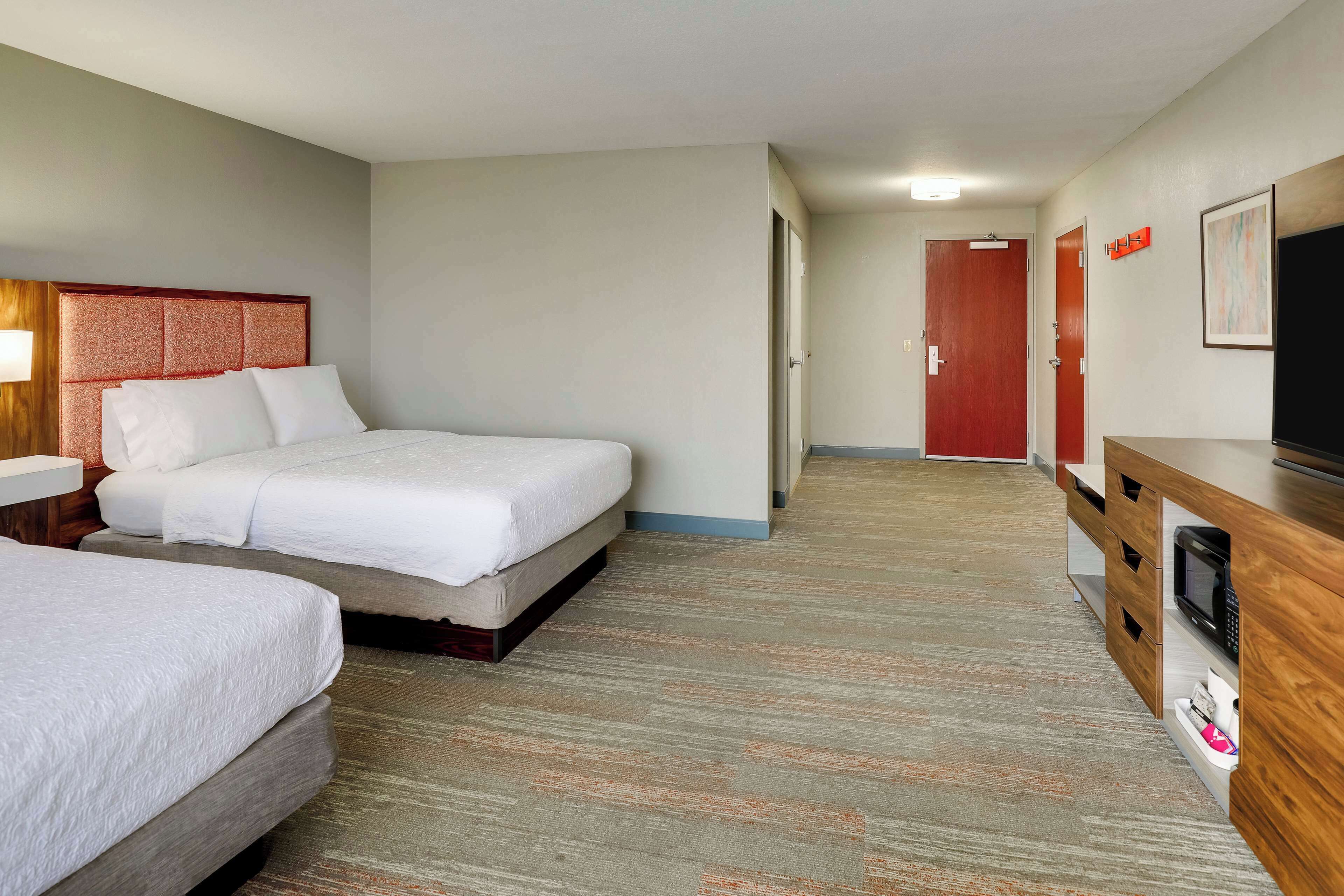 Habitación de hotel con dos camas, un escritorio de madera con televisión y un pasillo que conduce a una puerta.