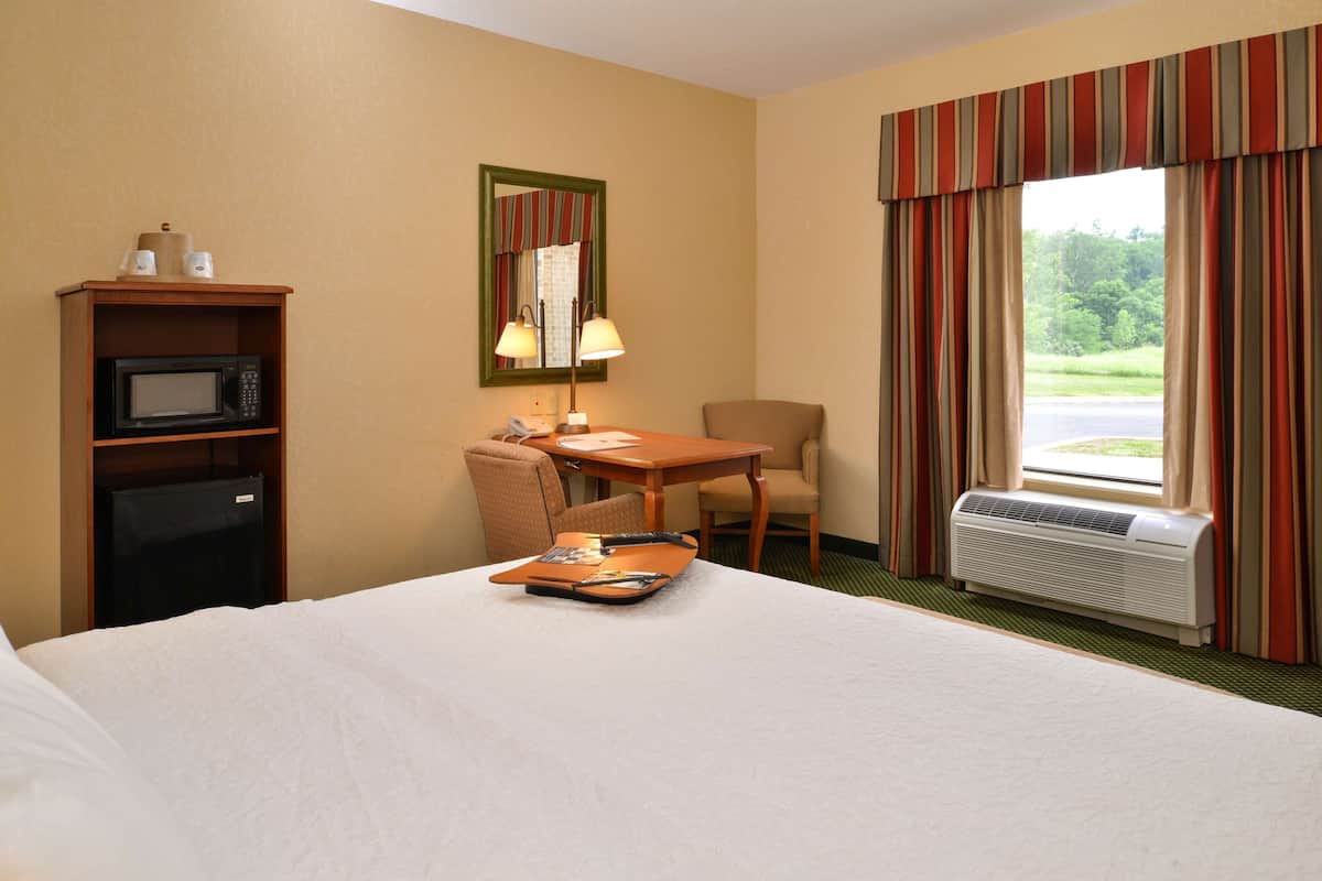 Habitación de hotel con cama, escritorio, silla, microondas, teléfono y ventana con cortinas.