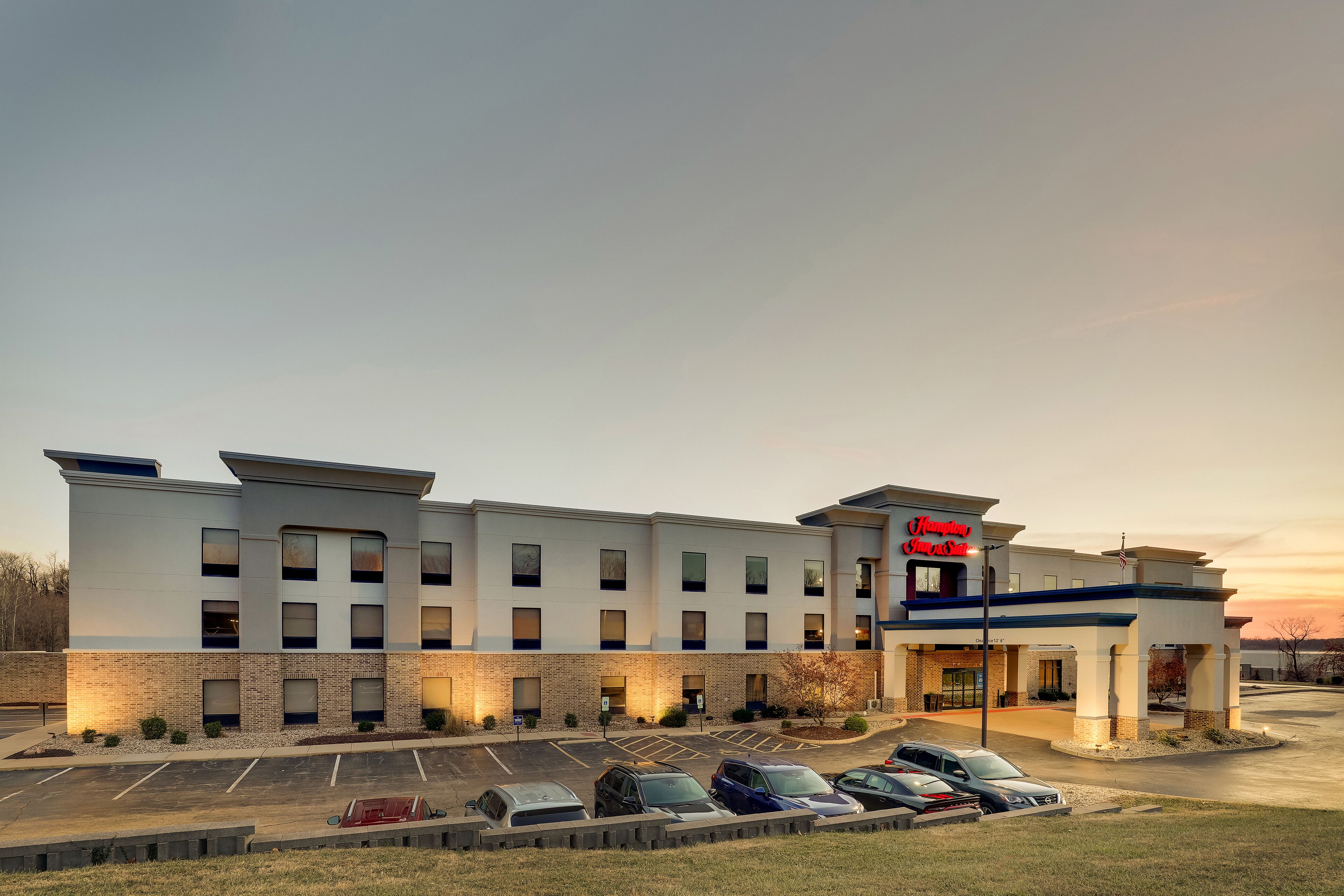 A modern hotel with a brick facade, multiple parking spaces, and a sign indicating it is a Hampton Inn & Suites.