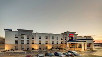 A modern hotel with a brick facade, multiple parking spaces, and a sign indicating it is a Hampton Inn & Suites.