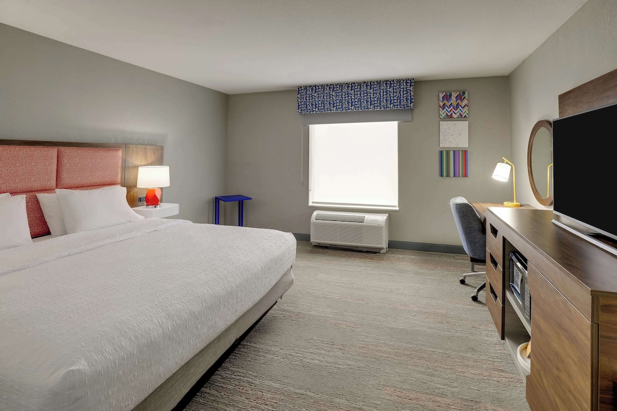 Habitación de hotel con una cama grande, un escritorio con computadora, un televisor y una ventana con vistas.