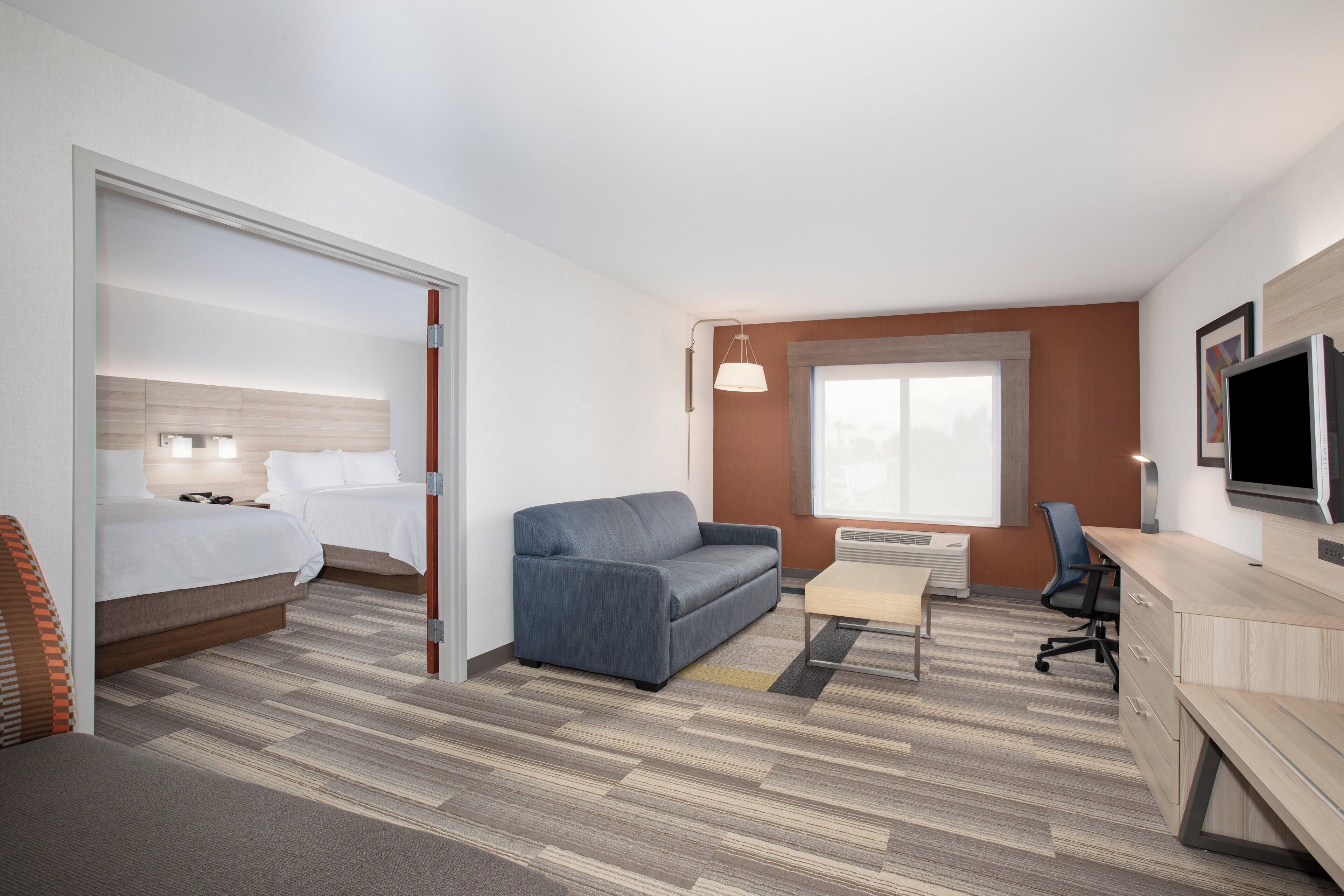 A hotel room with a bed, a sofa, a desk, a television, and a window.