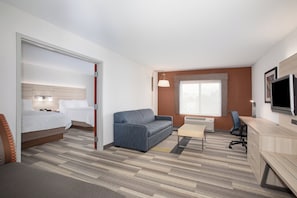 A hotel room with a bed, a sofa, a desk, a television, and a window.