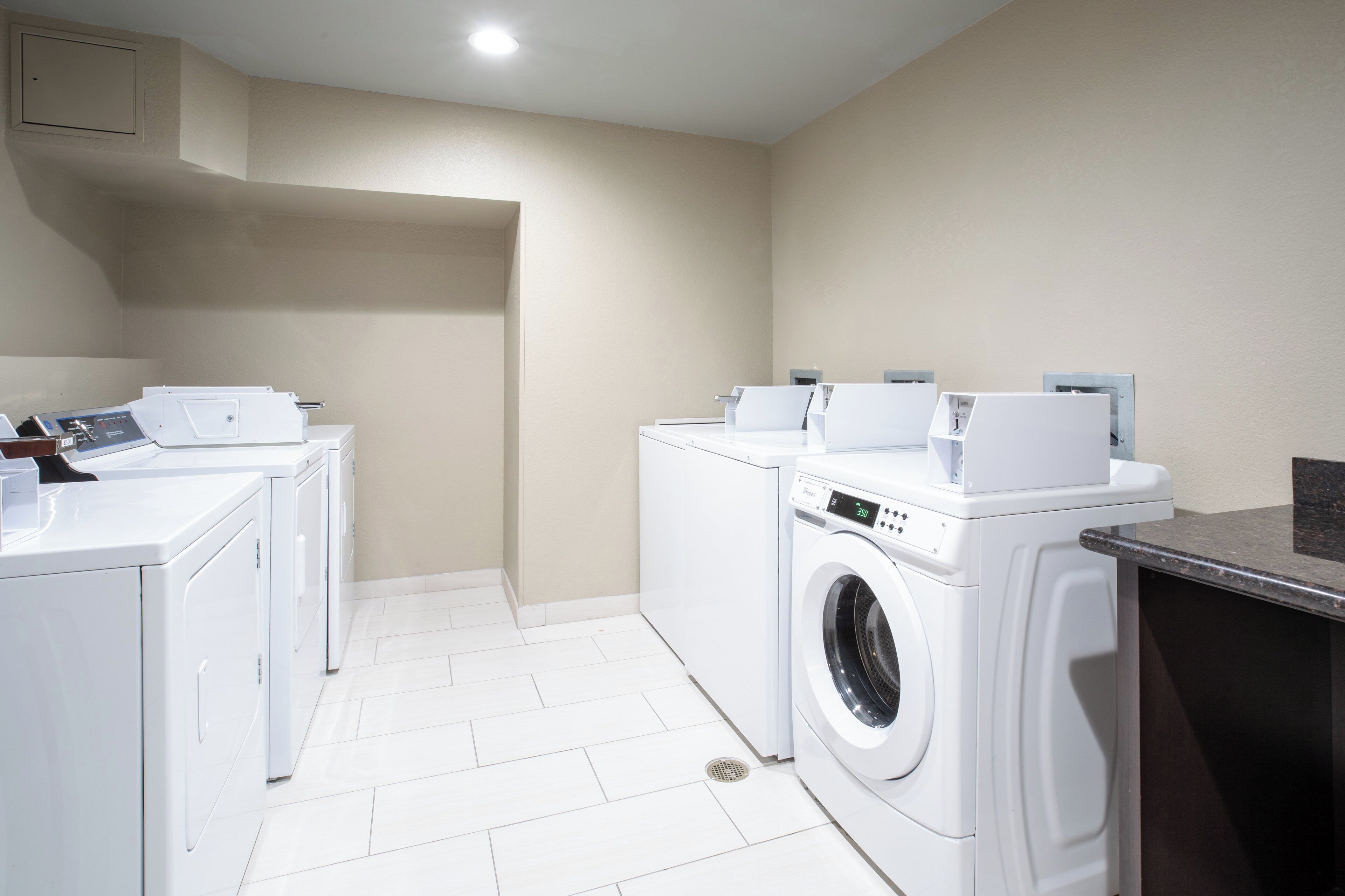 A laundry room with white appliances, including a washing machine and dryers, and a control panel.
