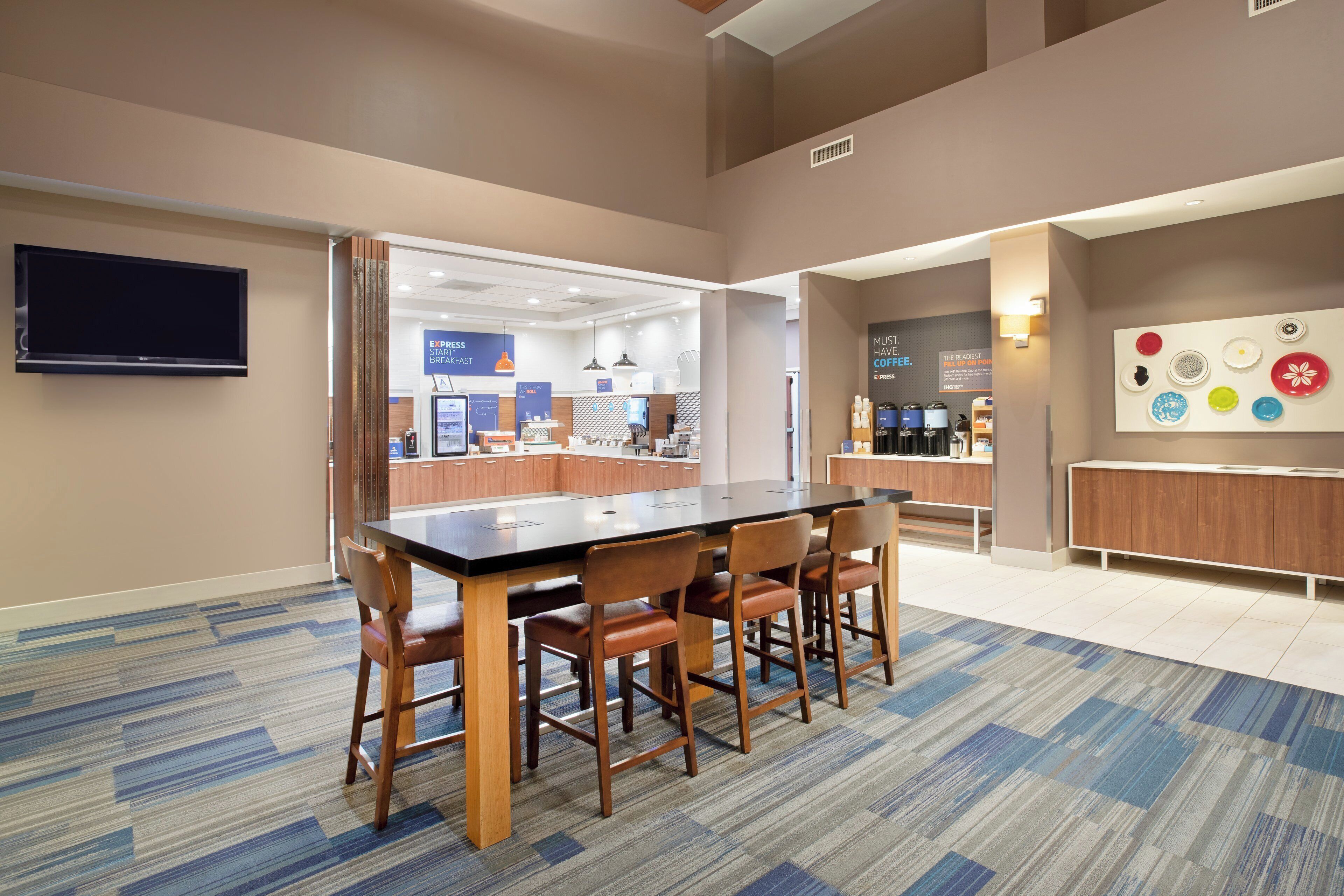 A conference room with a long table and chairs, a television mounted on the wall, and a coffee station with various cups and a kettle.
