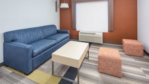 A modern room with a blue sofa, a wooden coffee table, and two patterned ottomans. - Holiday Inn Express and Suites Ontario Airport by IHG (Ontario)