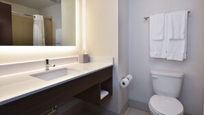 A bathroom with a white sink, a mirror, a towel rack with two towels, a toilet, and a roll of toilet paper.
