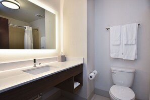 A bathroom with a white sink, a mirror, a towel rack with two towels, a toilet, and a roll of toilet paper.