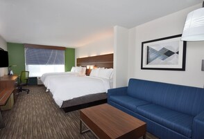 Una habitación de hotel con una cama, un sofá azul, una mesa de centro de madera, un escritorio y una silla.