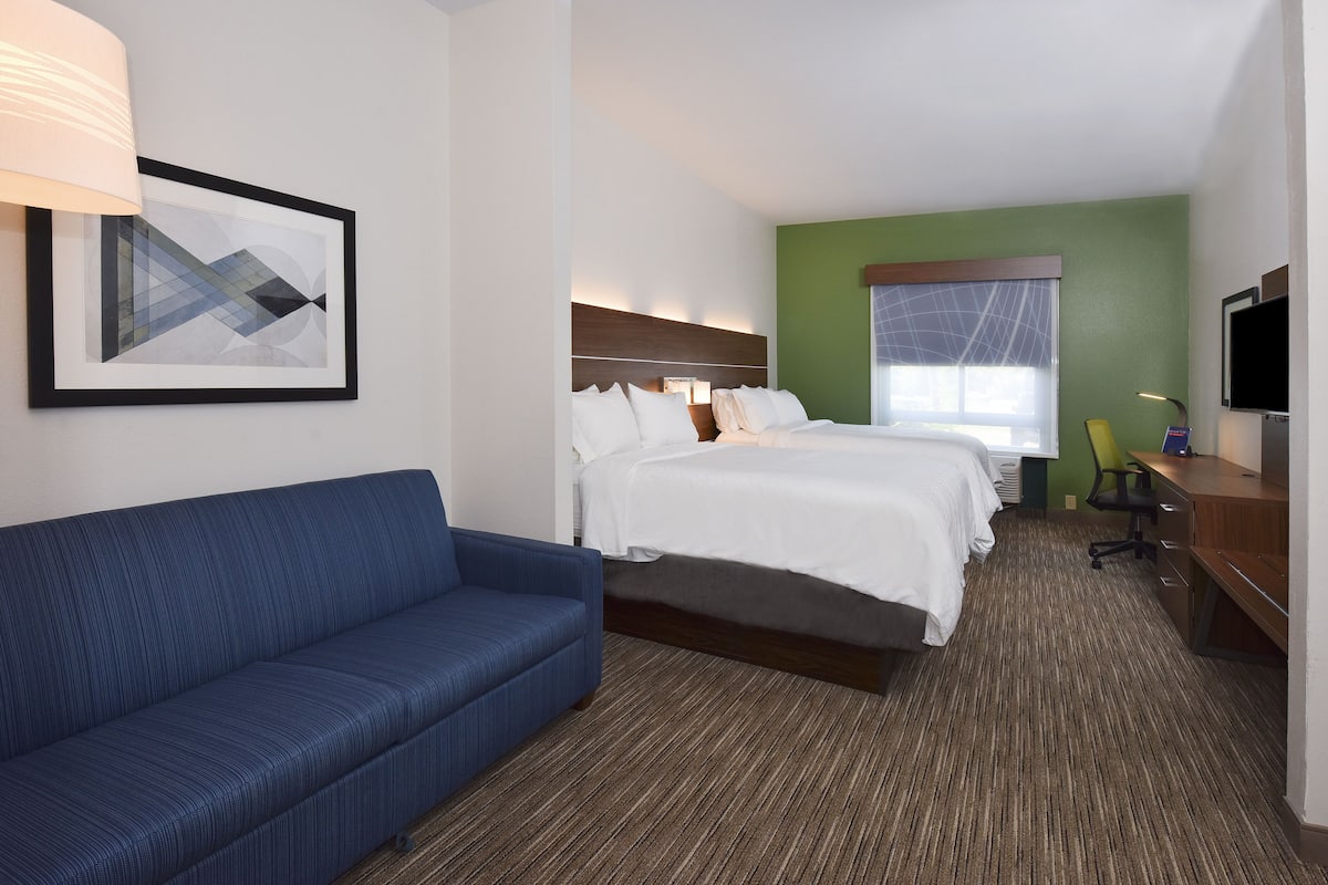 A hotel room with a bed, a blue sofa, a desk, a TV, and a framed picture on the wall.