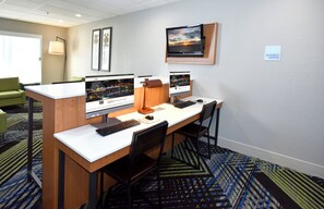 A hotel workspace with two desks, each with a computer, keyboard, and mouse. There are framed pictures on the wall, a lamp, and a sign indicating the business center. - Holiday Inn Express Selma by IHG (Selma)