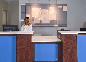 A reception desk with a modern design, a large illuminated sign above, and a computer monitor on the left. - Holiday Inn Express Selma by IHG (Selma)