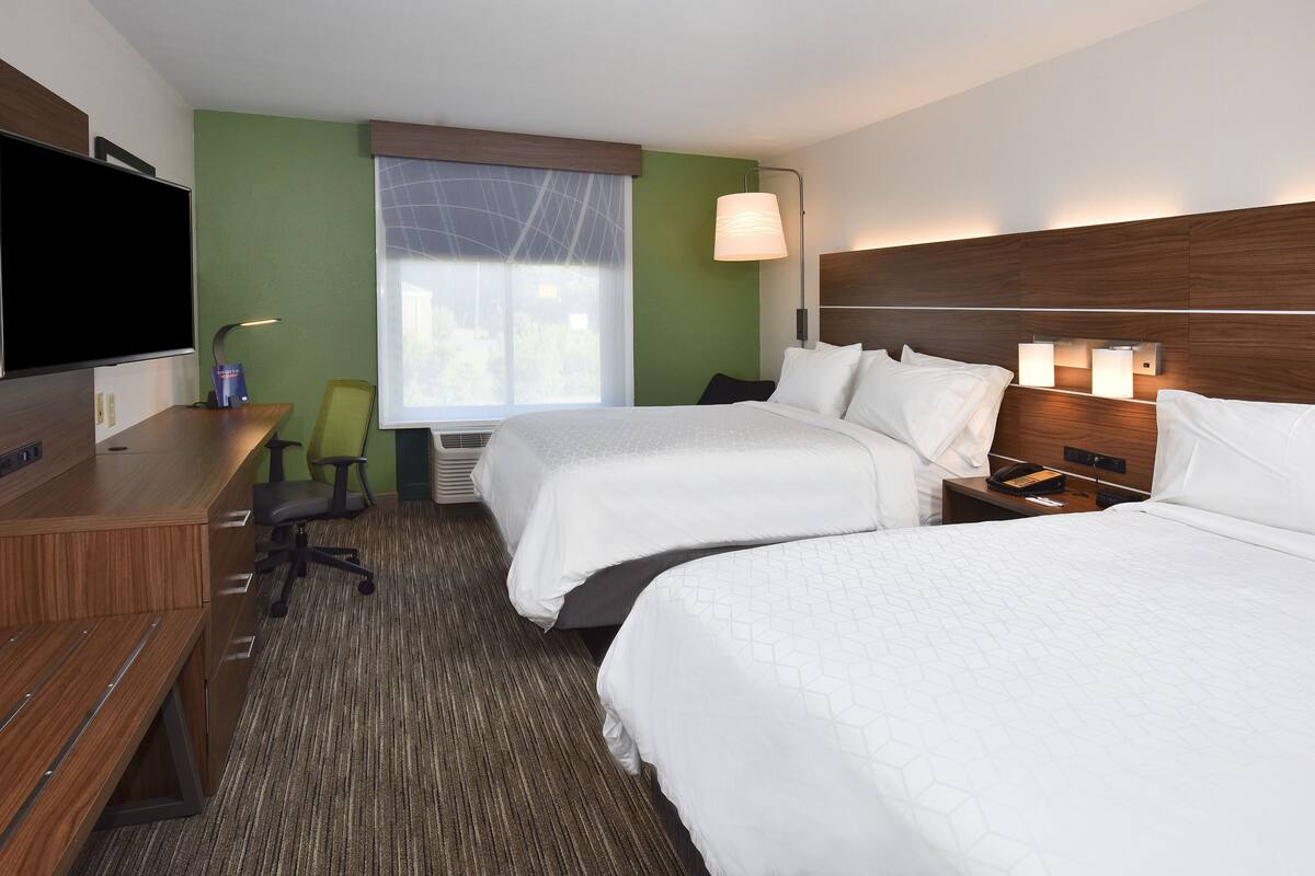 A hotel room with two beds, a desk, a chair, a TV, and a window with a view.