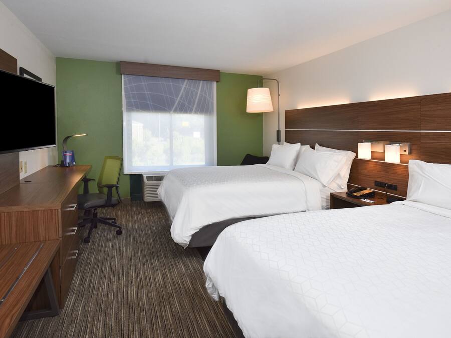 A hotel room with two beds, a desk, a chair, a TV, and a window with a view.