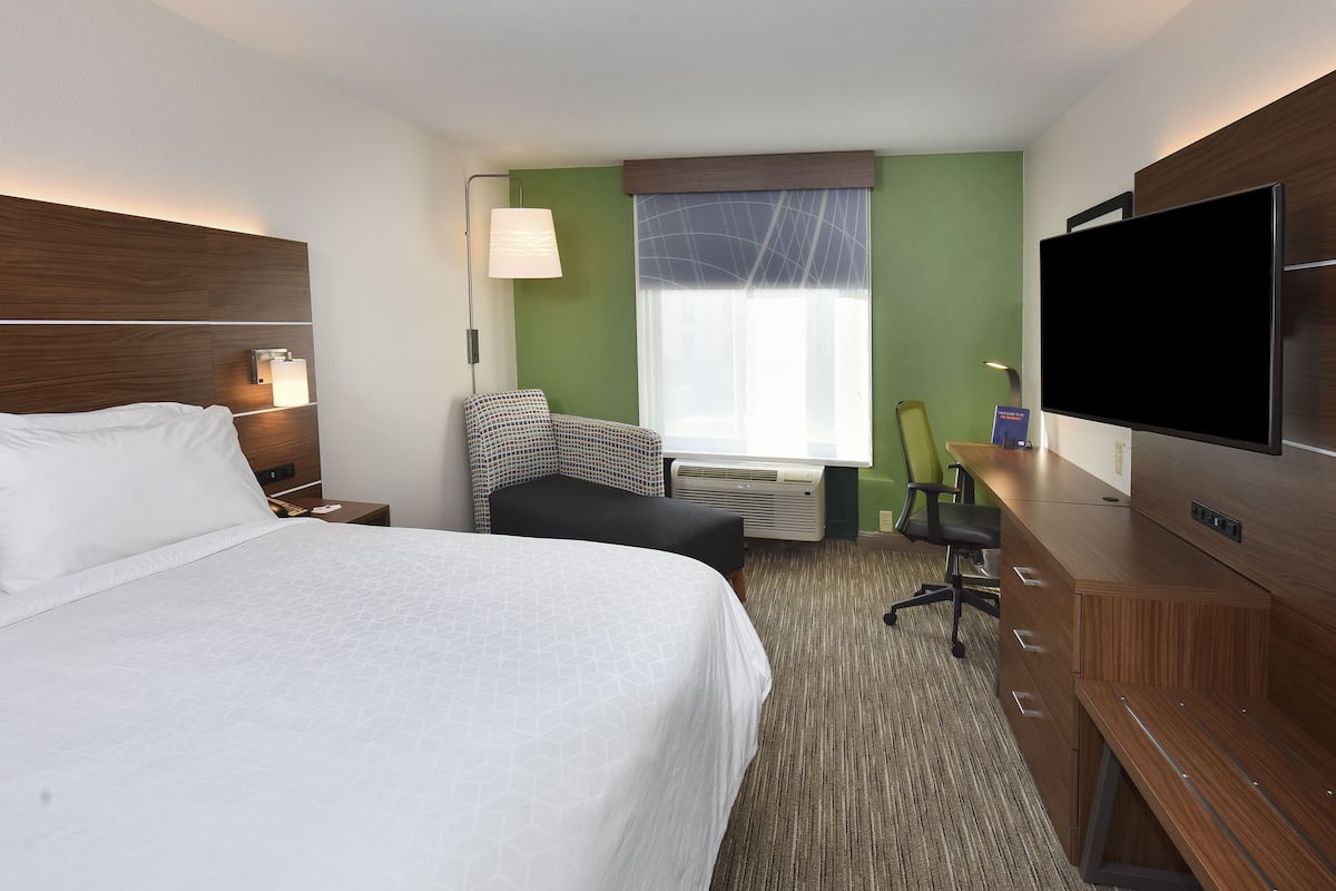 A hotel room with a large bed, a desk with a flat-screen TV, a chair, a lamp, and a window with a view.