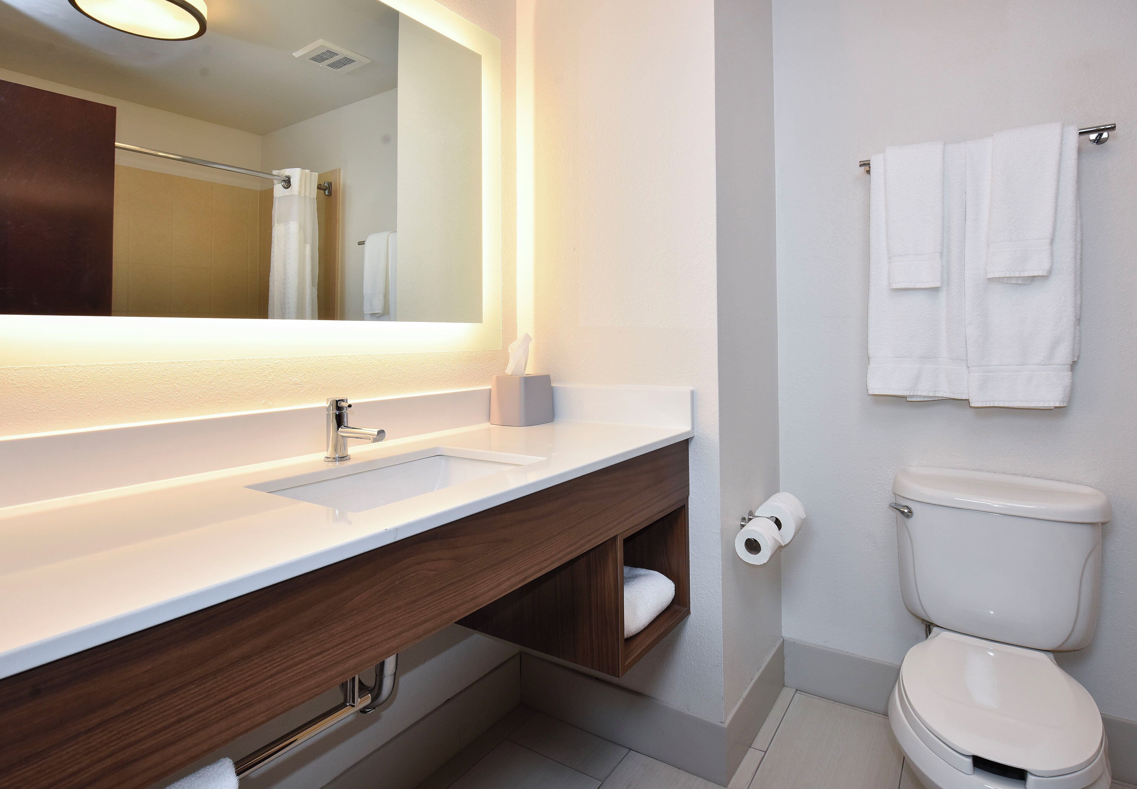 A modern bathroom with a white sink, a mirror, a toilet, and a towel rack.