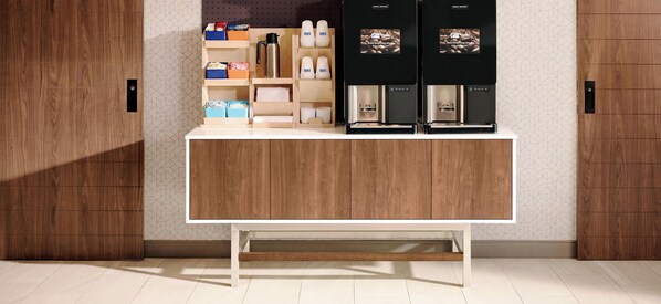 A modern kitchen area with wooden cabinetry, a coffee station with two coffee machines, and storage shelves with various items.