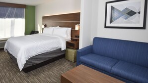 A hotel room with a bed, a blue sofa, a wooden nightstand, and a framed abstract artwork on the wall.