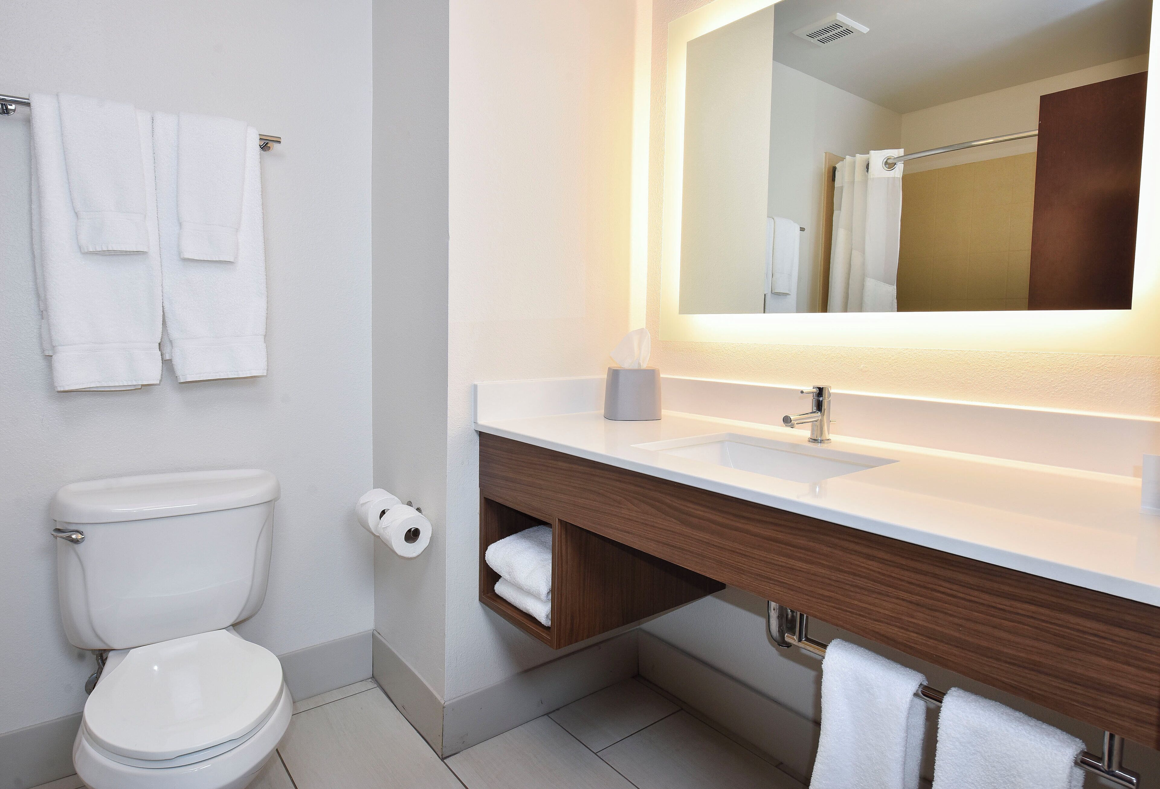 Un bagno moderno con un water, un lavandino, uno specchio e due asciugamani appesi al muro.