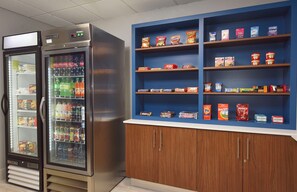 Una máquina expendedora con diversas bebidas y aperitivos, y un estante con alimentos envasados.
