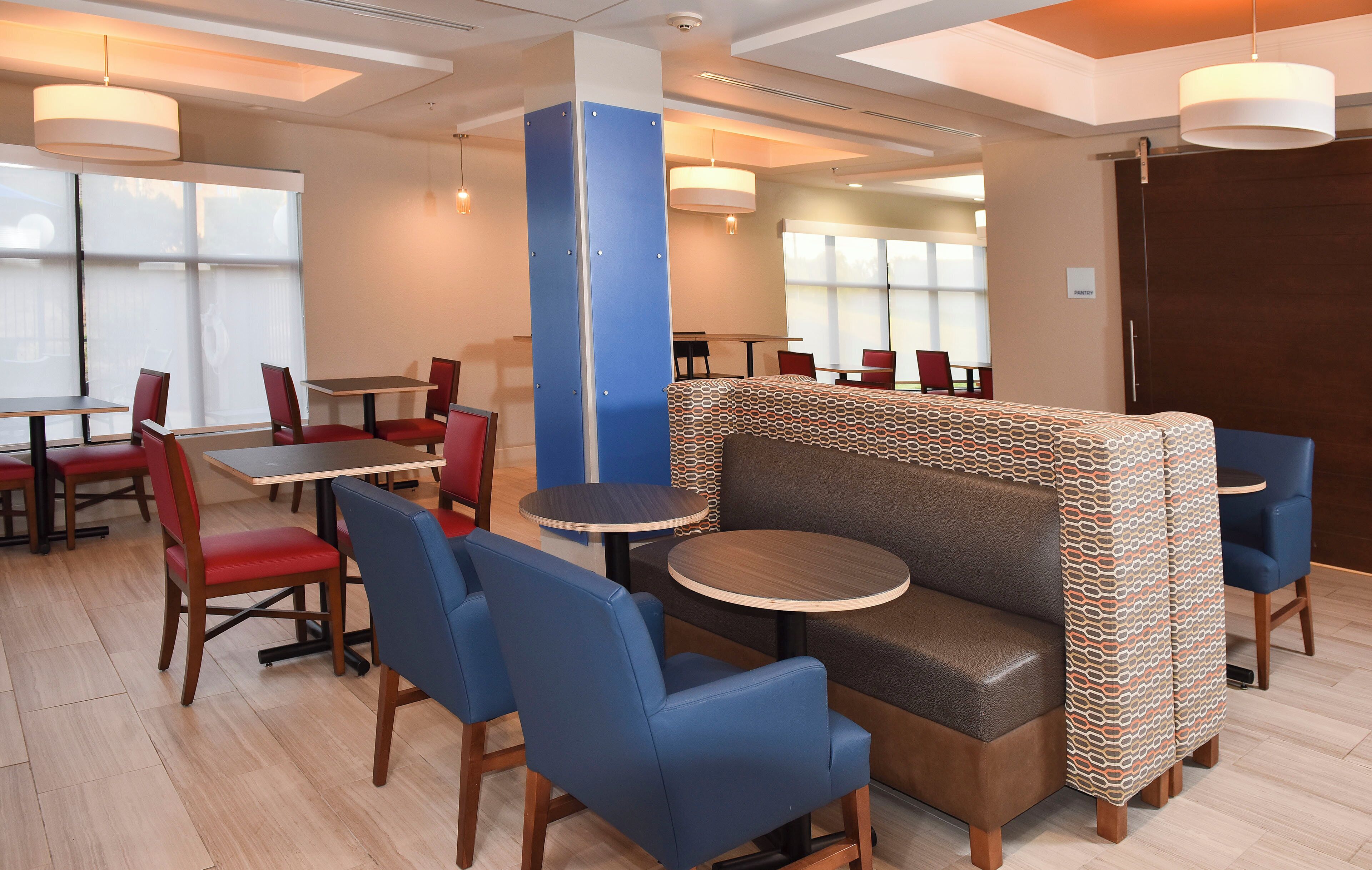 Un comedor moderno con asientos tipo cabina y mesas, una pared azul decorativa y un letrero que dice 'PANTRY'.