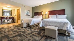 Habitación de hotel con dos camas, una zona de estar, un tocador con espejo y un cuadro en la pared.