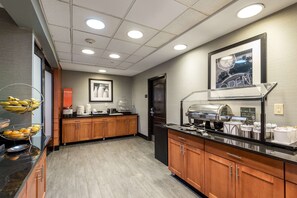 Una cocina de hotel con armarios de madera, encimera negra y barra de desayuno con estación de café.