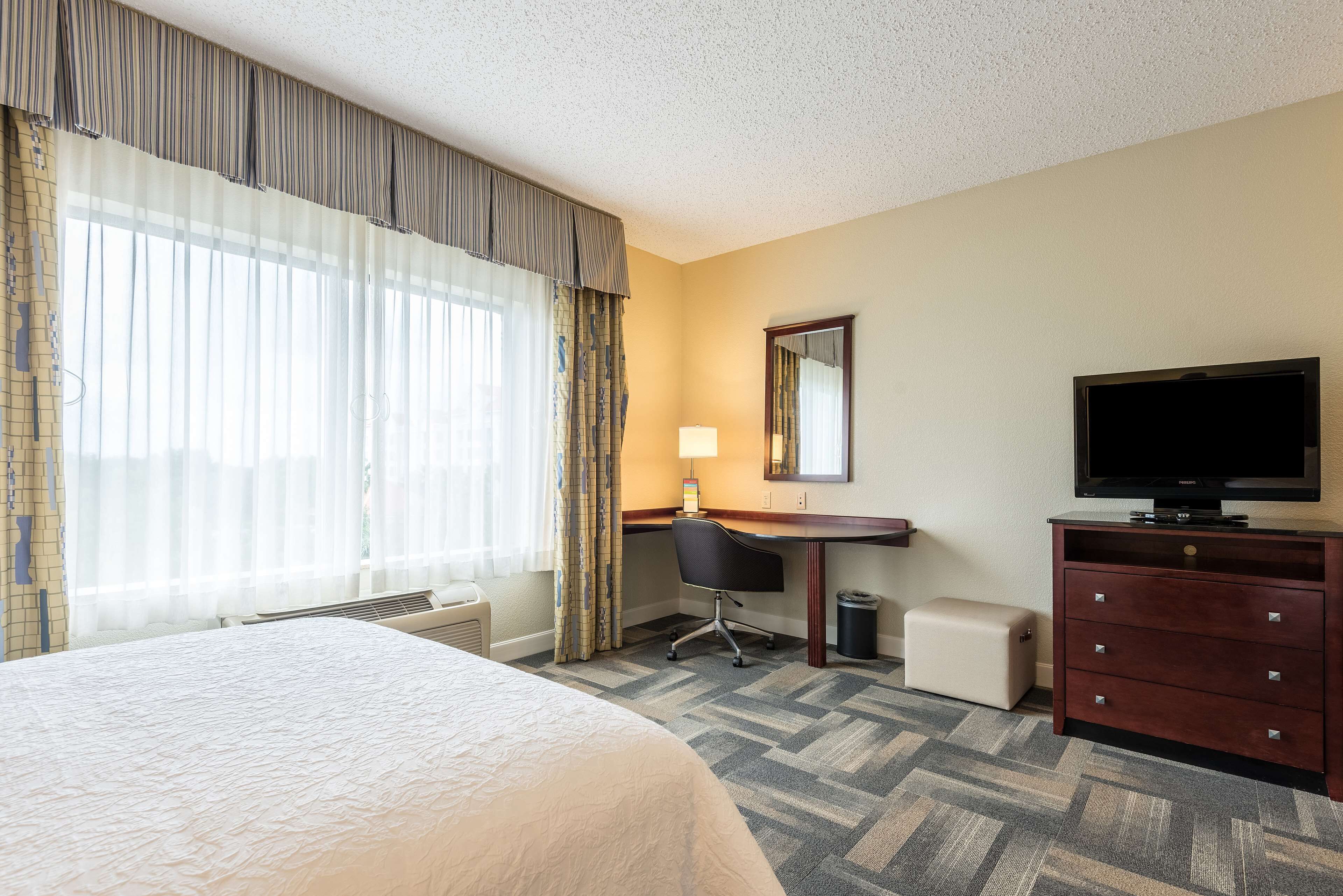 A hotel room with a bed, a desk, a chair, a television, and a dresser.