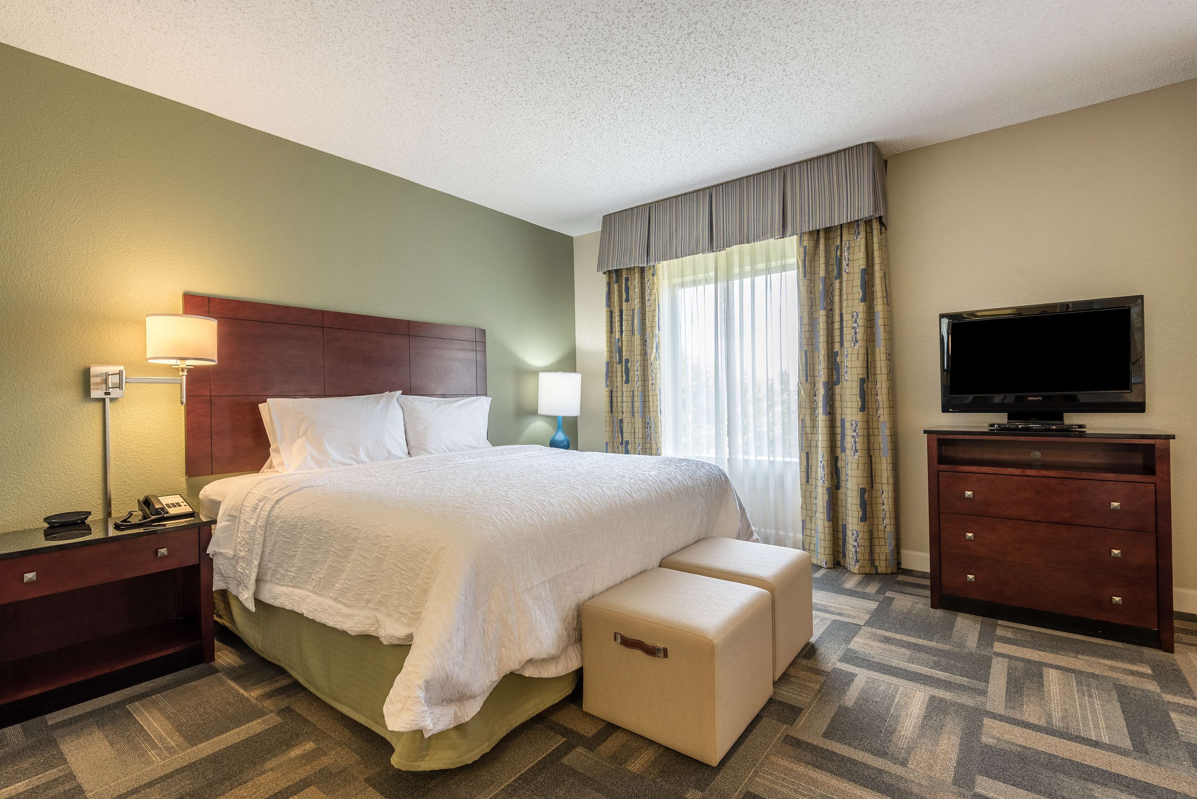A hotel room with a large bed, a bedside table, a lamp, a TV, and a dresser.